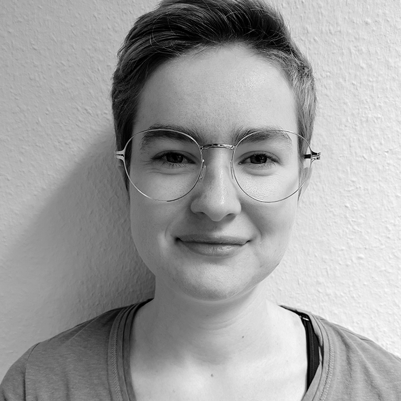Das Portraitbild zeigt die Mitarbeiterin Benedikte Löbbert. Sie hat kurze Haare und eine Brille mit goldenem Rand. Sie lächelt leicht in die Kamera.